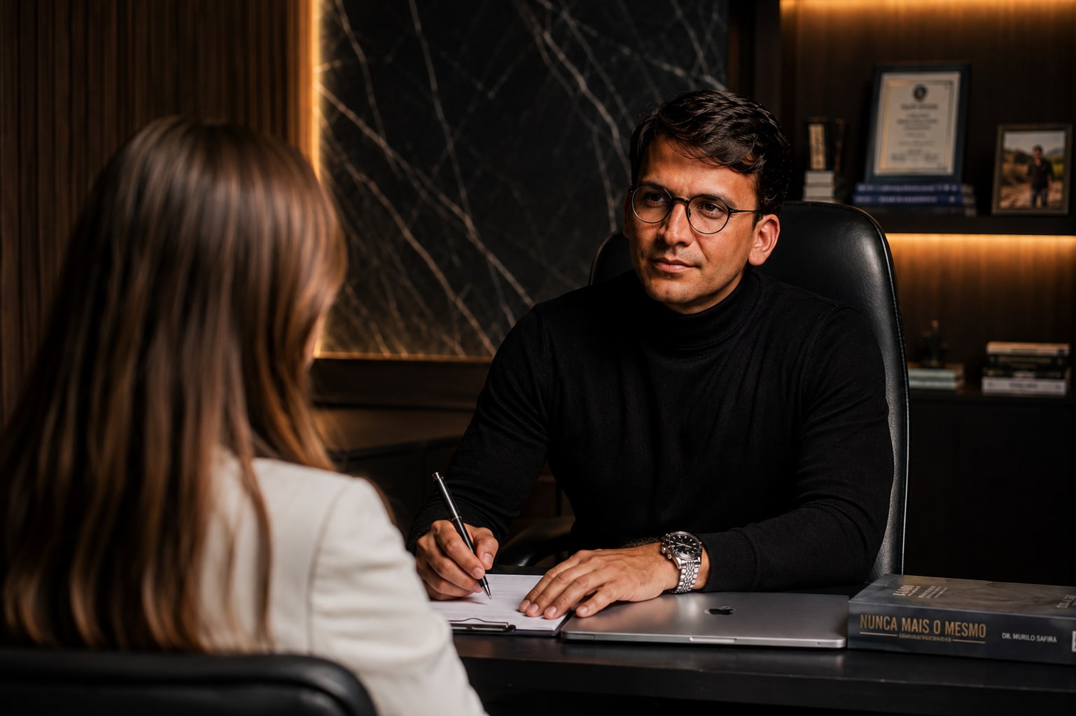 Dr. Murilo Safira em consulta, escrevendo enquanto ouve a paciente.